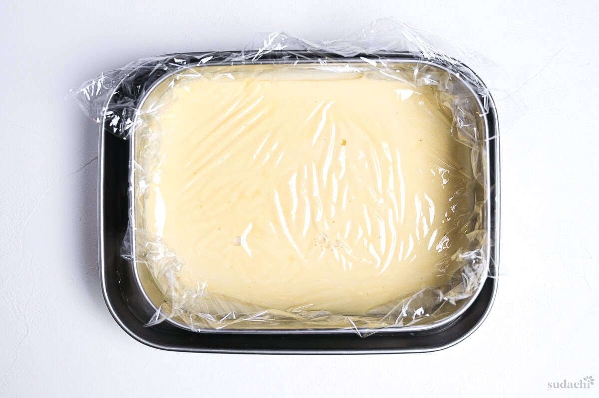 hojicha ice cream mixture in a steel container covered with plastic wrap during cooling