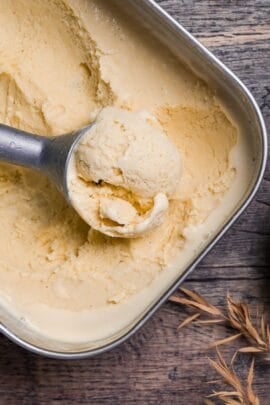 Homemade hojicha ice cream scooped in a steel container next to loose hojicha tea stems in a brown bowl