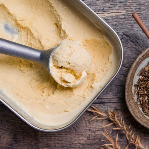 Homemade hojicha ice cream scooped in a steel container next to loose hojicha tea stems in a brown bowl