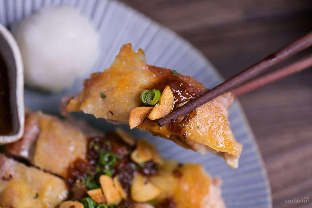 A piece of pan fried Japanese chicken steak held up with wooden chopsticks