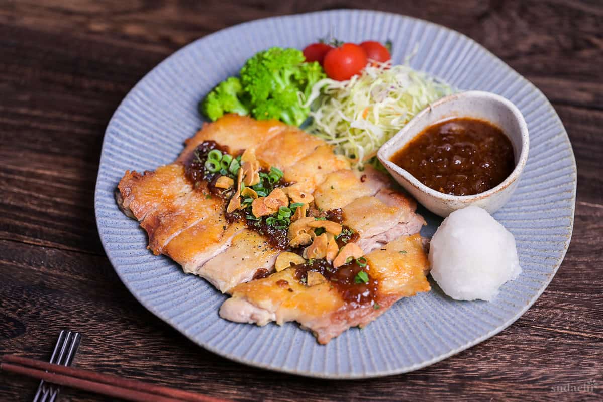 Japanese style pan fried chicken steak with homemade sauce and crispy garlic chips on a blue plate side view