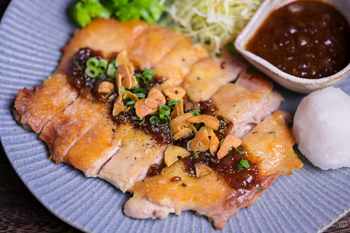 Japanese style pan fried chicken steak with homemade sauce and crispy garlic chips on a blue plate close up