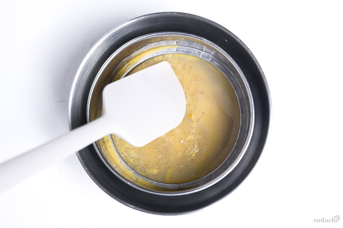 whisked egg strained through a fine-mesh strainer into a steel mixing bowl