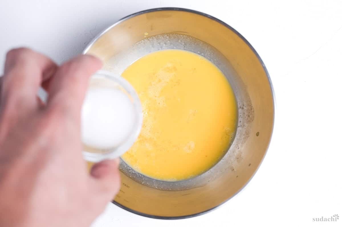 adding slurry to whisked egg in a steel mixing bowl