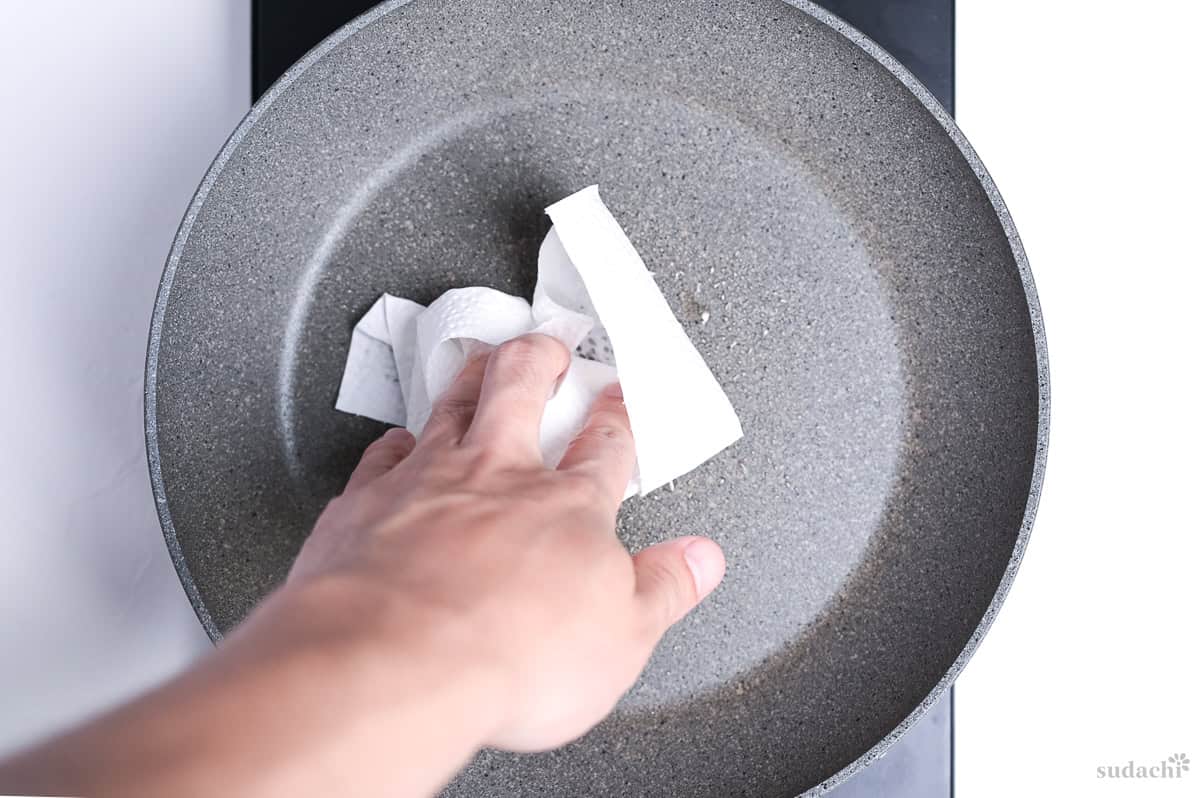 wiping a thin layer of oil into a pan using a piece of kitchen paper