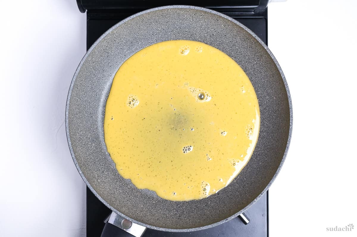 kinshi tamago (Japanese shredded egg crepe) frying in a thin layer in a gray frying pan on the stove top