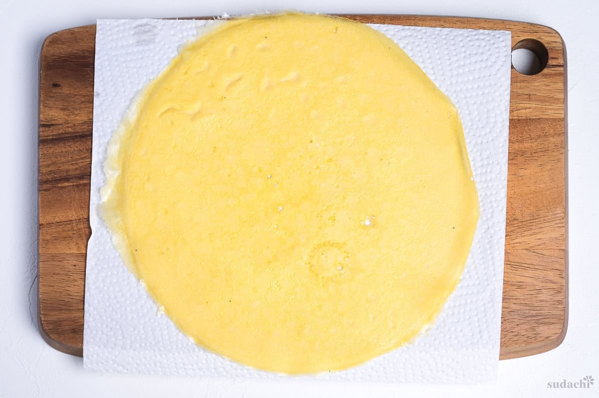 Kinshi tamago (Japanese shredded egg crepe) on a piece of kitchen paper over a wooden cutting board before cutting