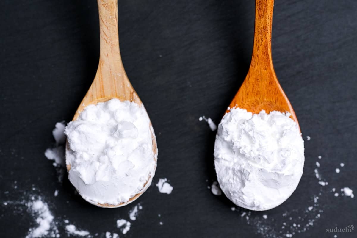 Potato starch on a light wooden spoon, and cornstarch on a darker wooden spoon side by side on a wooden cutting board