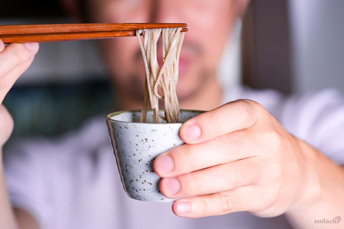 Yuto Omura holding up soba noodles dipped in a homemade cold sesame dipping sauce