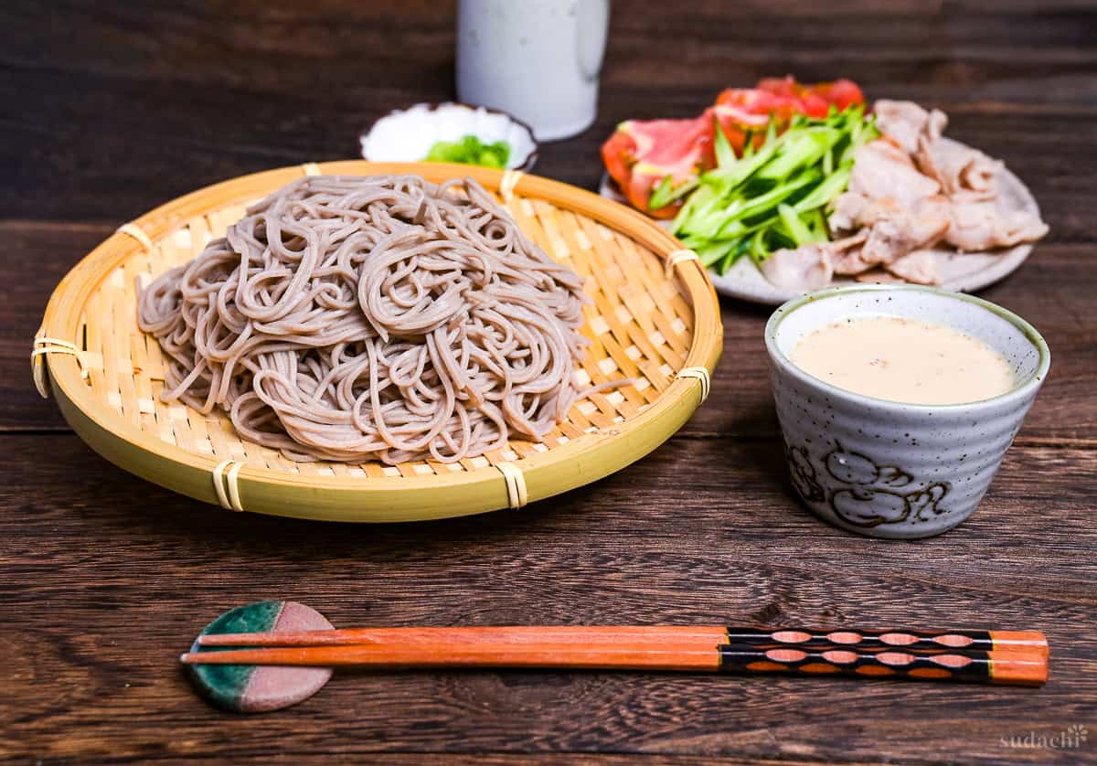 Cooked and cooled soba noodles on a bamboo tray (zaru) next to a small bowl of homemade sesame dipping sauce