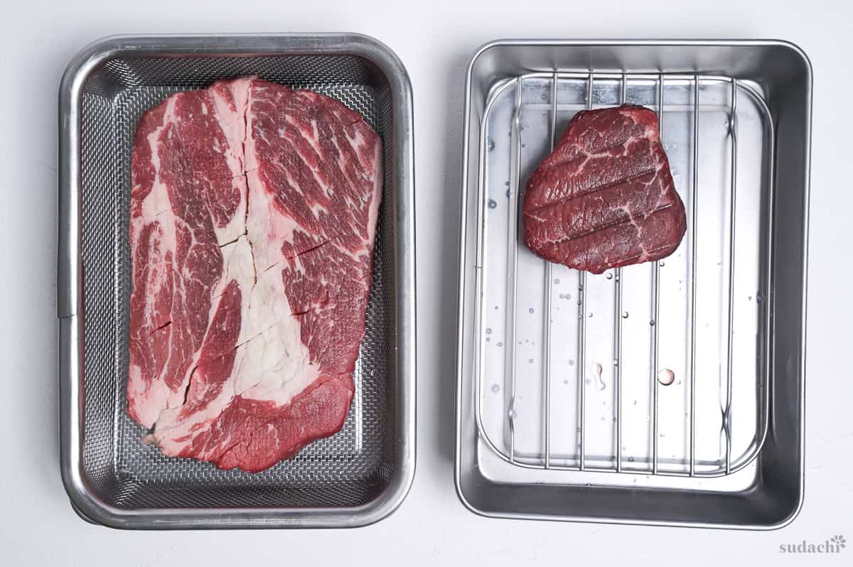 Salted beef steaks on wire racks in steel containers to draw out excess moisture and soften the meat (overnight rest).