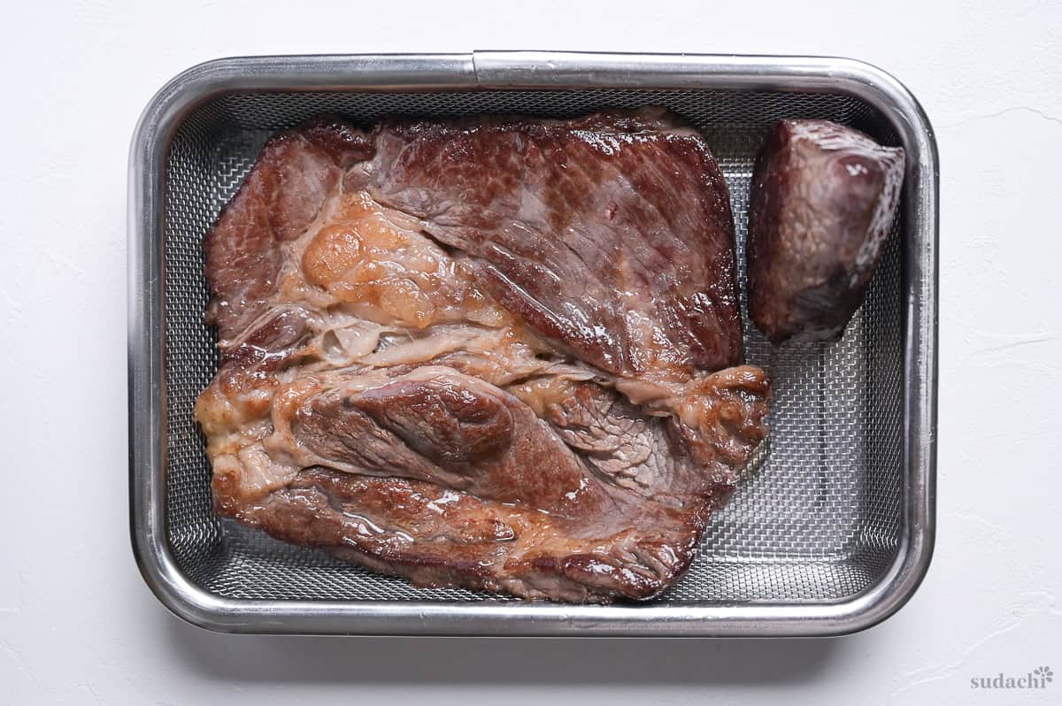 Pan fried steak resting on a wire rack over a steel container.