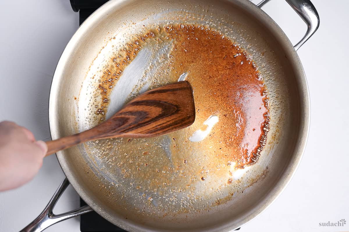 Deglazing a large pan after frying steak and garlic on the stove top.