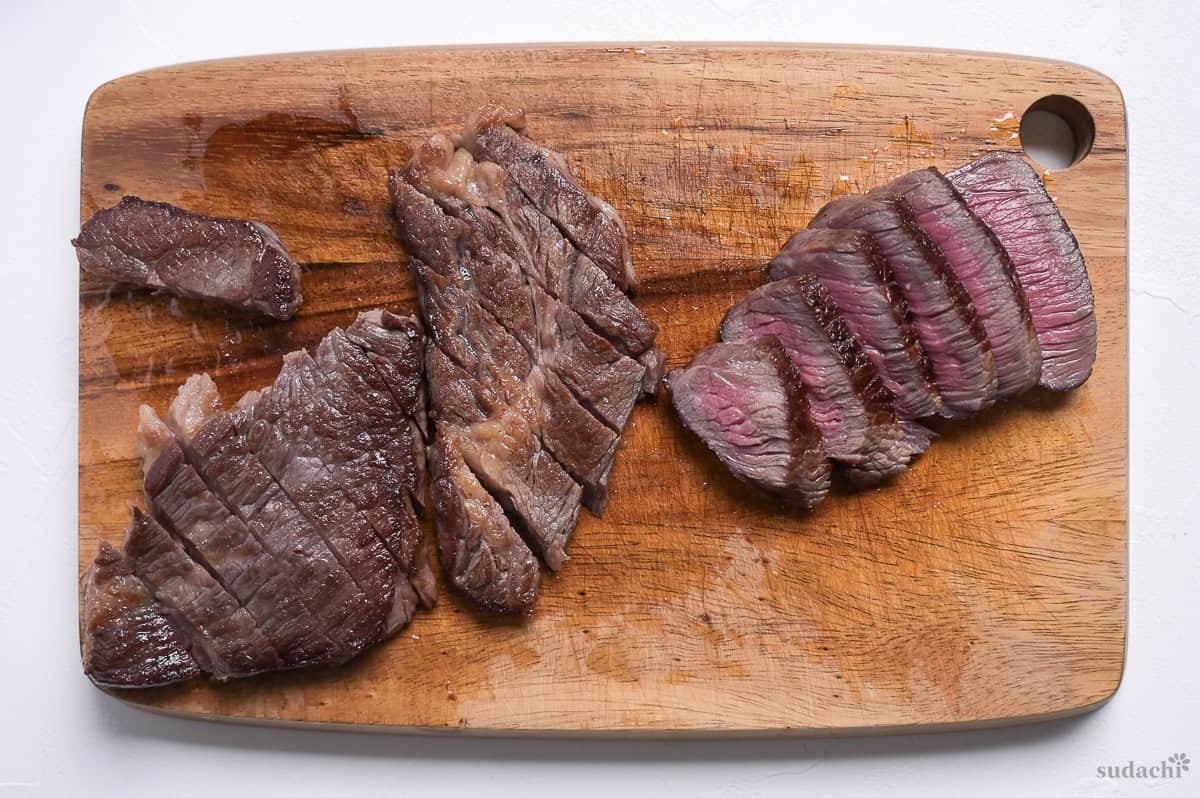 pan fried medium rare beef steaks sliced on a wooden cutting board