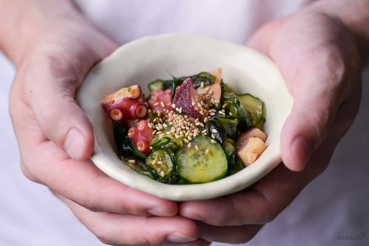 Yuto Omura holding octopus and cucumber sunomono salad topped with toasted white sesame seeds in a cream bowl