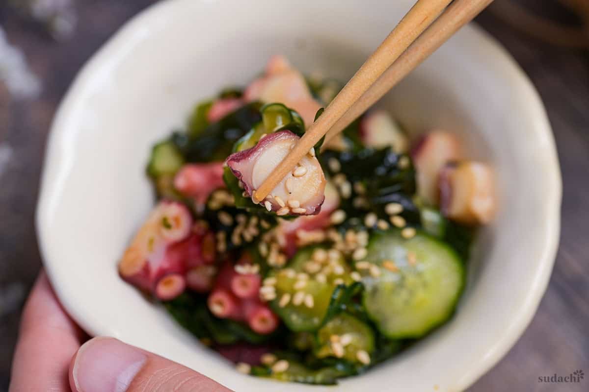 Octopus and cucumber sunomono salad held up with light wooden chopsticks
