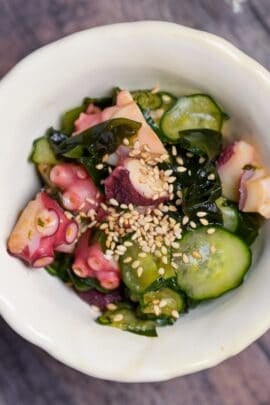 Japanese octopus and cucumber sunomono topped with toasted sesame seeds in an off-white ceramic bowl