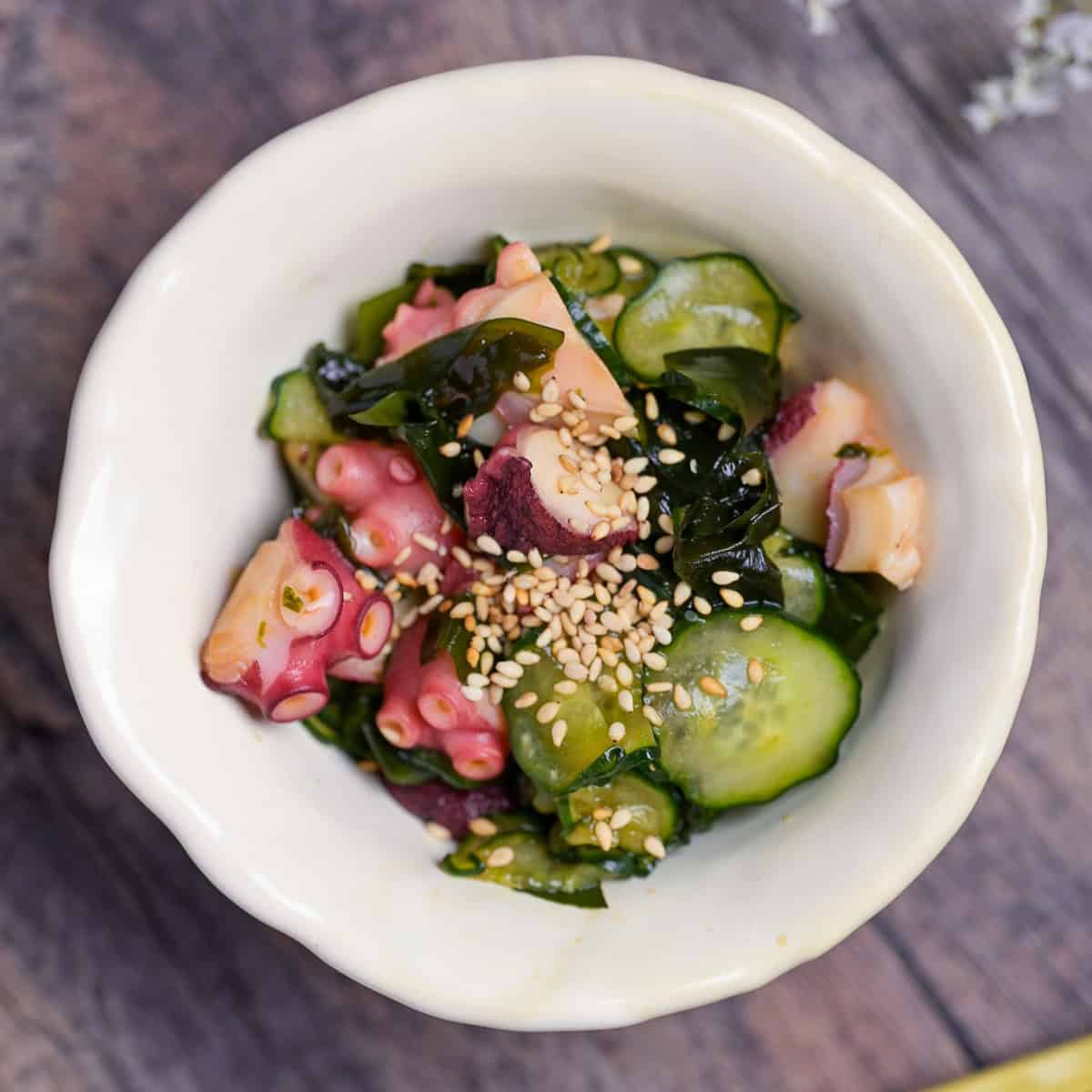 Japanese octopus and cucumber sunomono topped with toasted sesame seeds in an off-white ceramic bowl