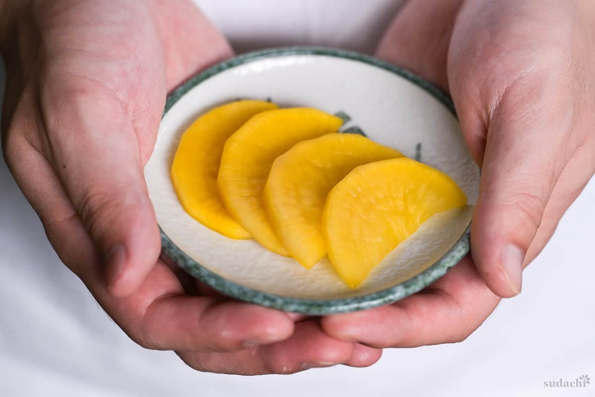 Yuto Omura holding four pieces of homemade shortcut takuan on a white plate with green rim