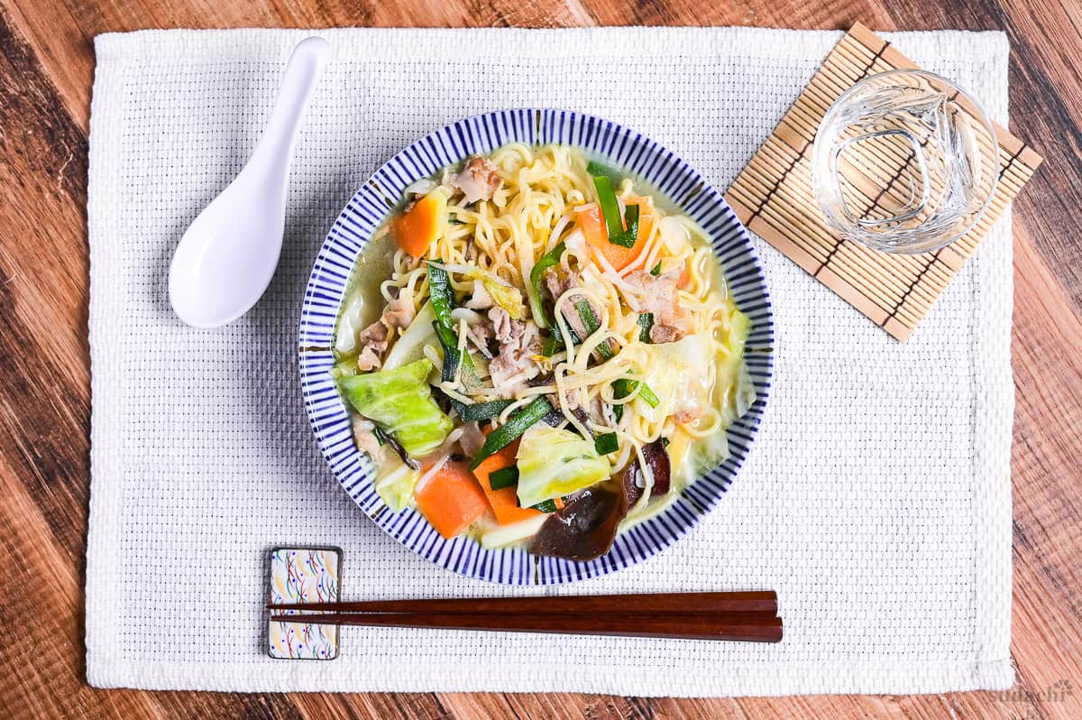 Japanese tanmen noodles in a white bowl with blue striped edge on a woven placemat.