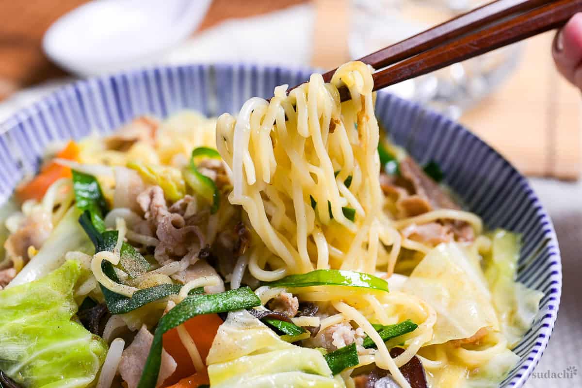 Close up of tanmen noodles being lifted with wooden chopsticks.