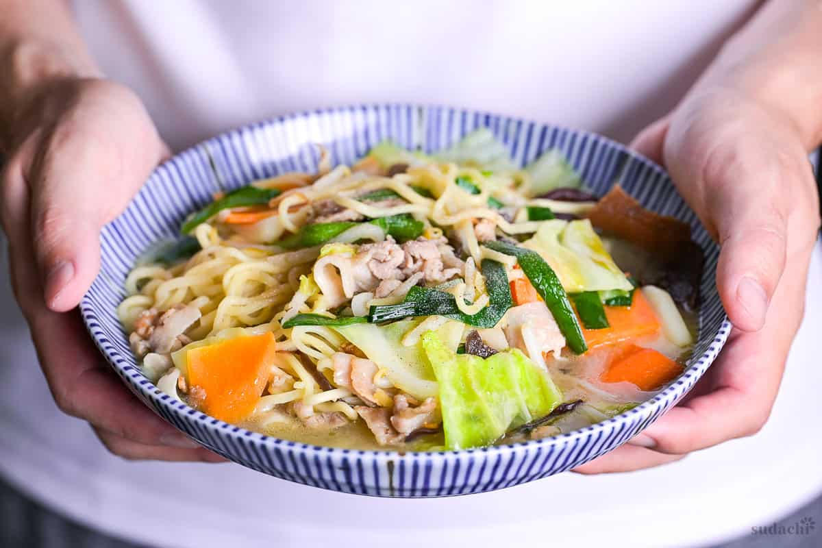 Yuto Omura holding up a bowl of tanmen made with ramen noodles, pork belly and vegetables in a chicken stock-based broth.