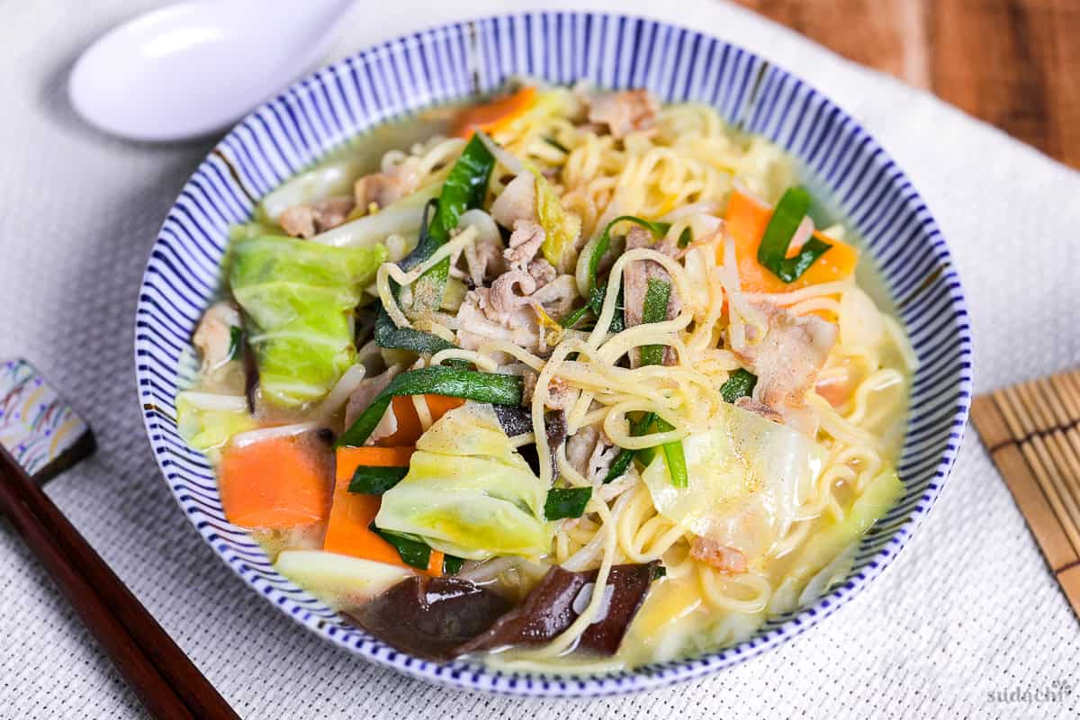 Japanese tanmen noodles in a white bowl with blue striped edge on a woven placemat.
