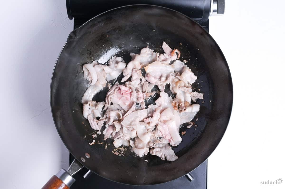seared thinly sliced pork belly in a wok on the stove top.