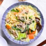 Japanese tanmen noodles in a white bowl with blue striped edge on a woven placemat.