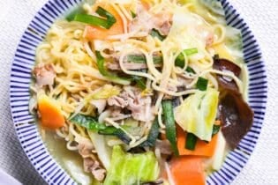 Japanese tanmen noodles in a white bowl with blue striped edge on a woven placemat.