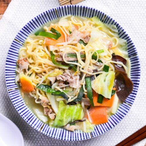 Japanese tanmen noodles in a white bowl with blue striped edge on a woven placemat.