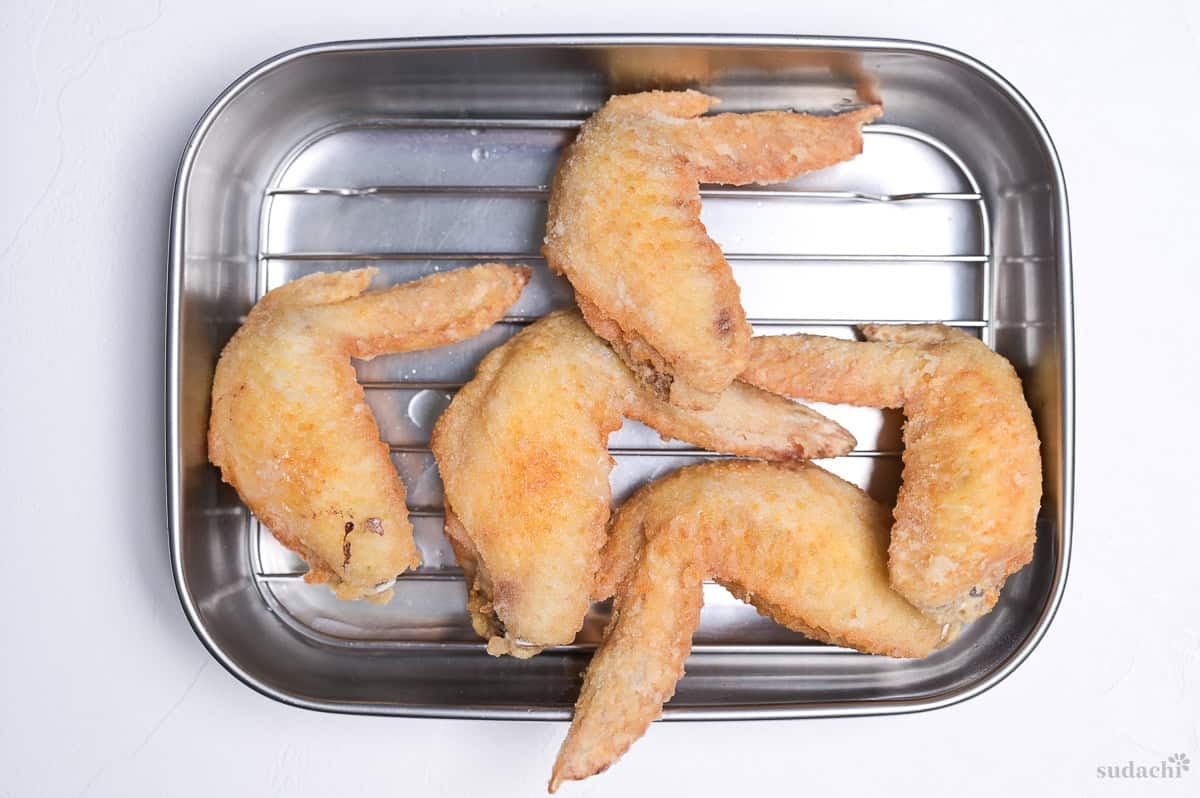 Fried whole chicken wings resting on a wire rack after frying