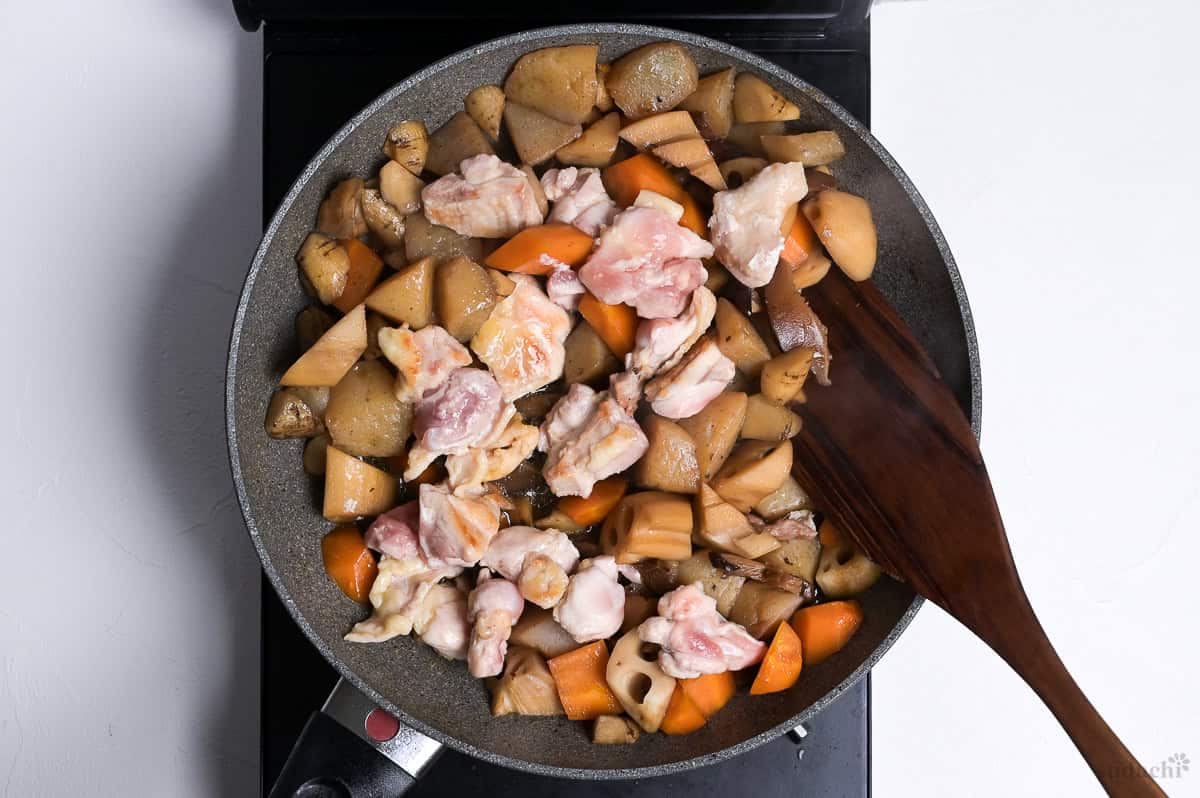 chikuzenni simmering with partially cooked chicken thigh pieces in a wide pan on the stove top