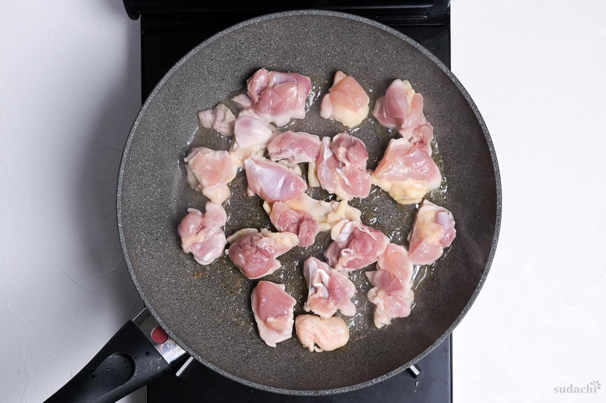 searing bitesize pieces of chicken thigh in a frying pan to make chikuzenni