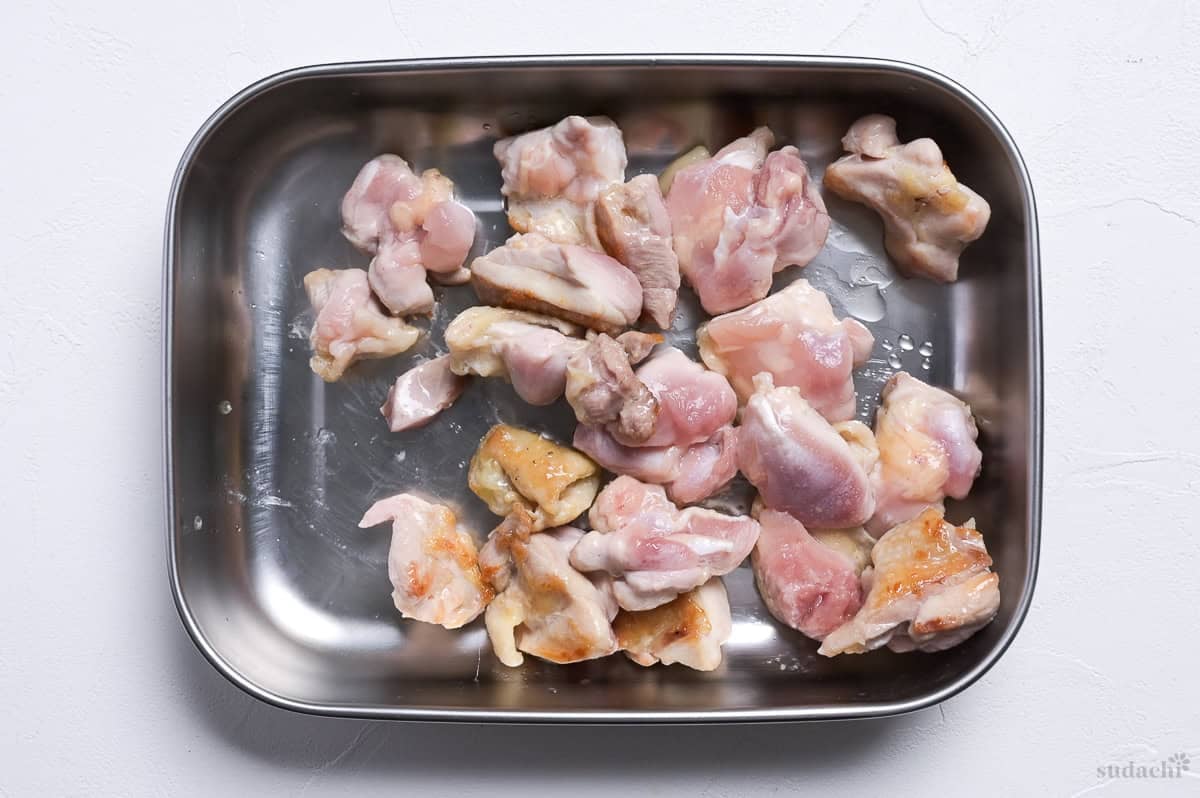 partially cooked chicken thigh pieces in a steel container