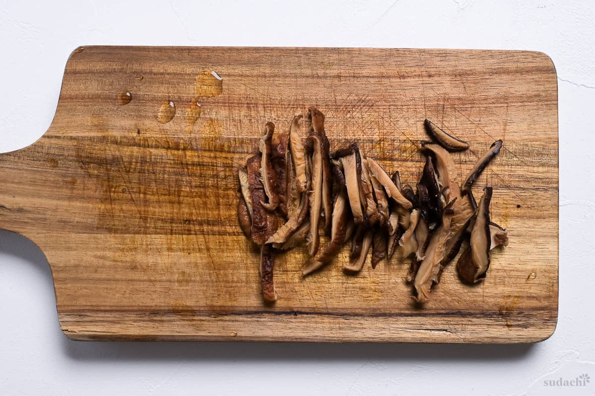 thinly sliced rehydrated shiitake mushrooms on a wooden cutting board