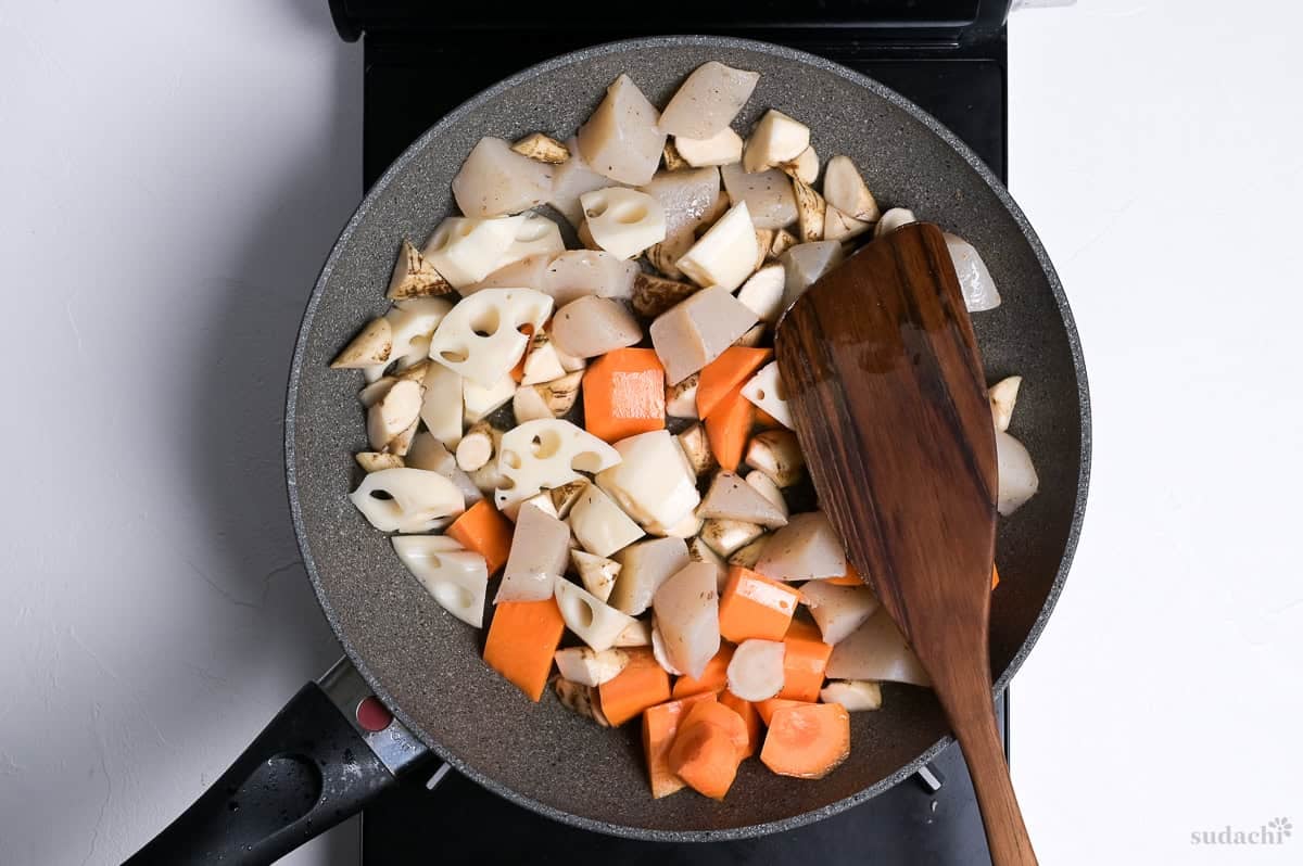 konnyaku and root vegetables cut into bitesize pieces in a frying pan with wooden spatula