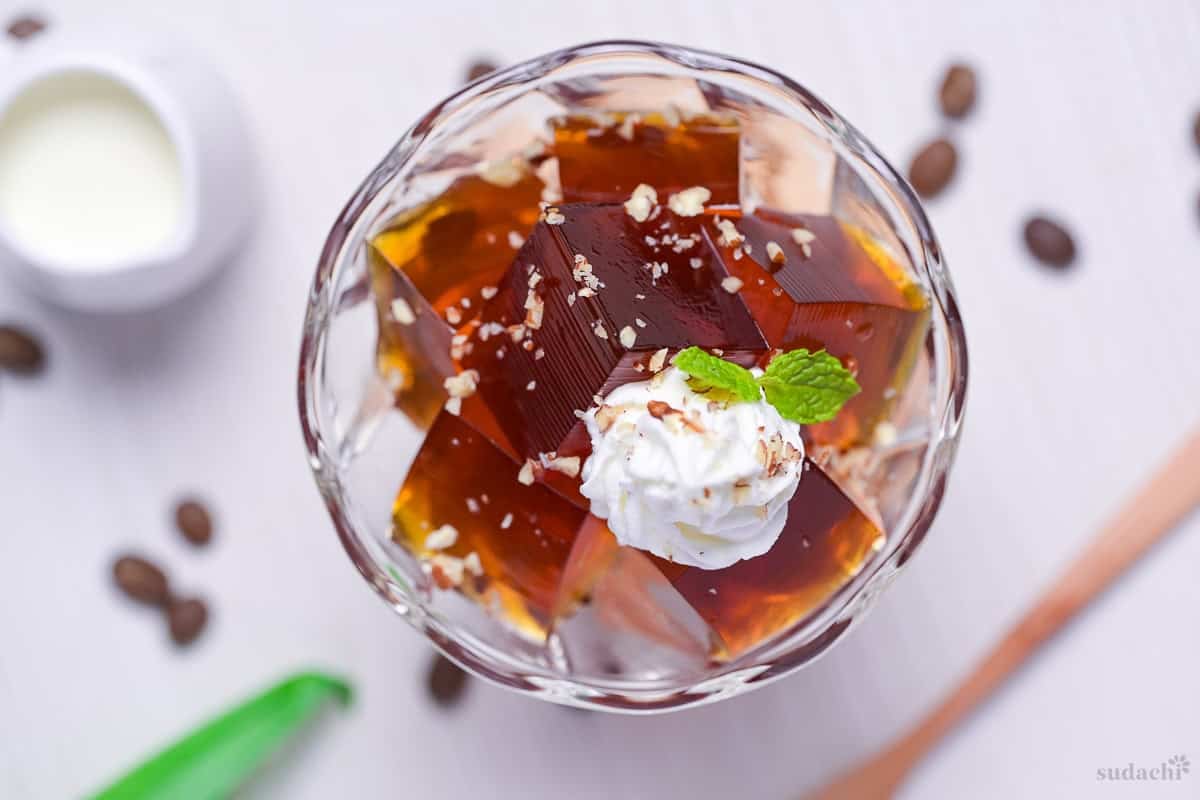 Cubes of Japanese coffee jelly topped with whipped cream, chopped nuts and a mint leaf served in a glass bowl