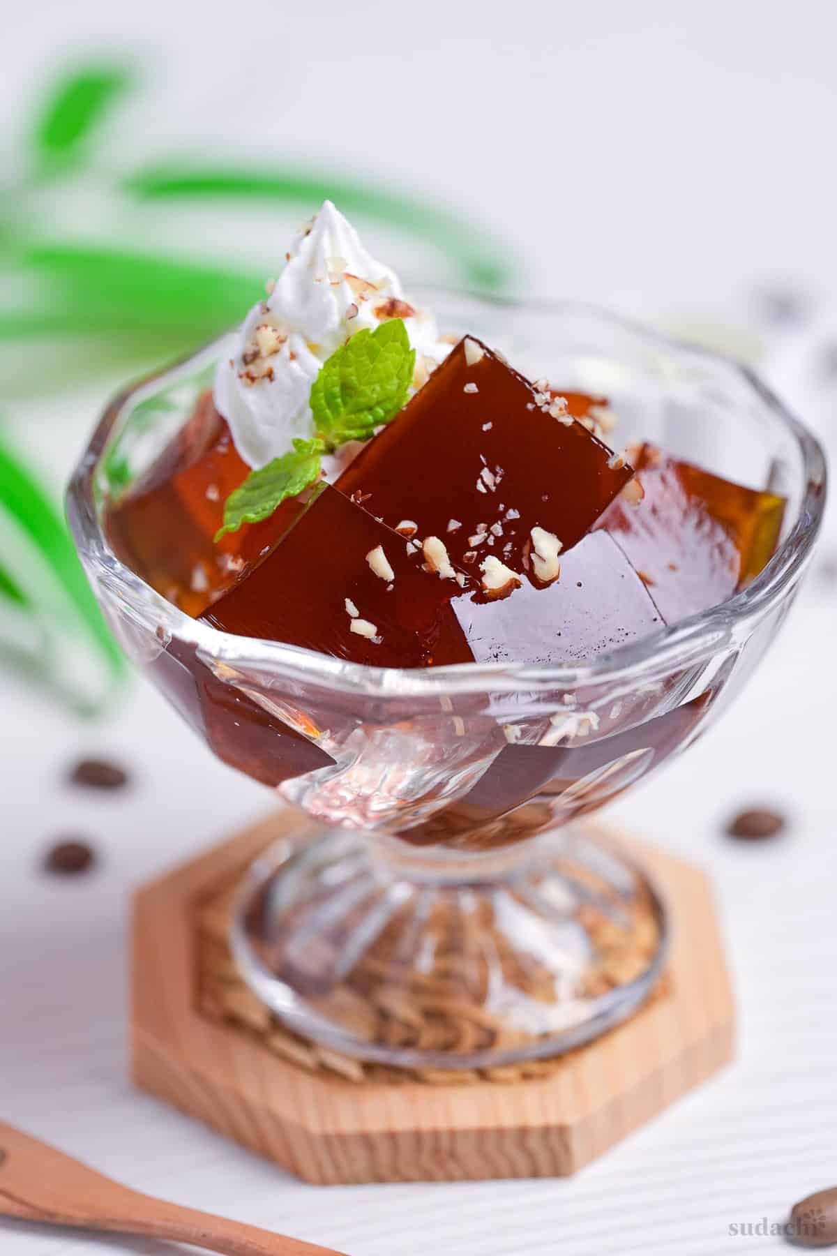 Cubes of Japanese coffee jelly topped with whipped cream, chopped nuts and a mint leaf served in a glass bowl