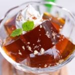 Cubes of Japanese coffee jelly topped with whipped cream, chopped nuts and a mint leaf served in a glass bowl