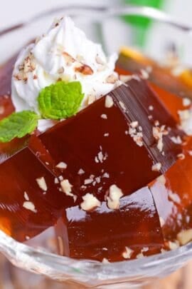 Cubes of Japanese coffee jelly topped with whipped cream, chopped nuts and a mint leaf served in a glass bowl