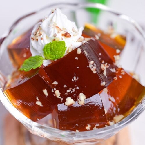 Cubes of Japanese coffee jelly topped with whipped cream, chopped nuts and a mint leaf served in a glass bowl
