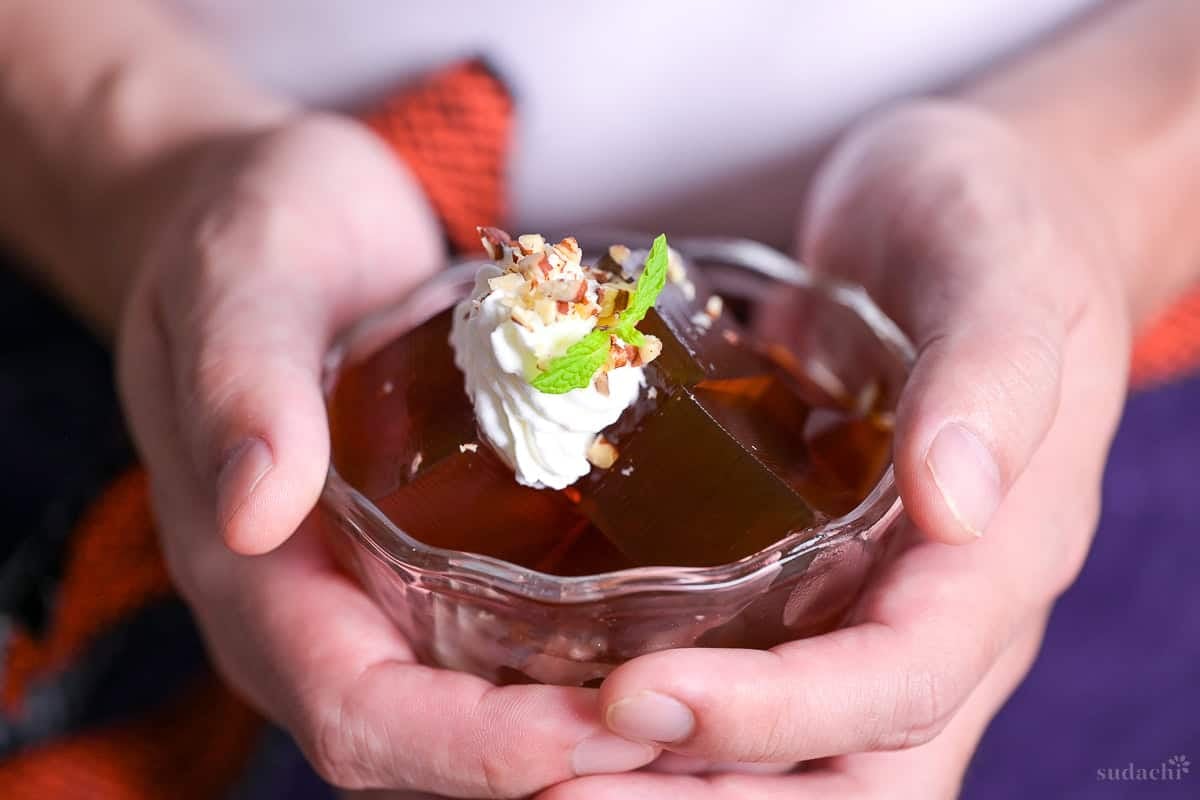 Yuto Omura holding up a bowl of cubed coffee jelly topped with whipped cream, chopped nuts and a mint leaf