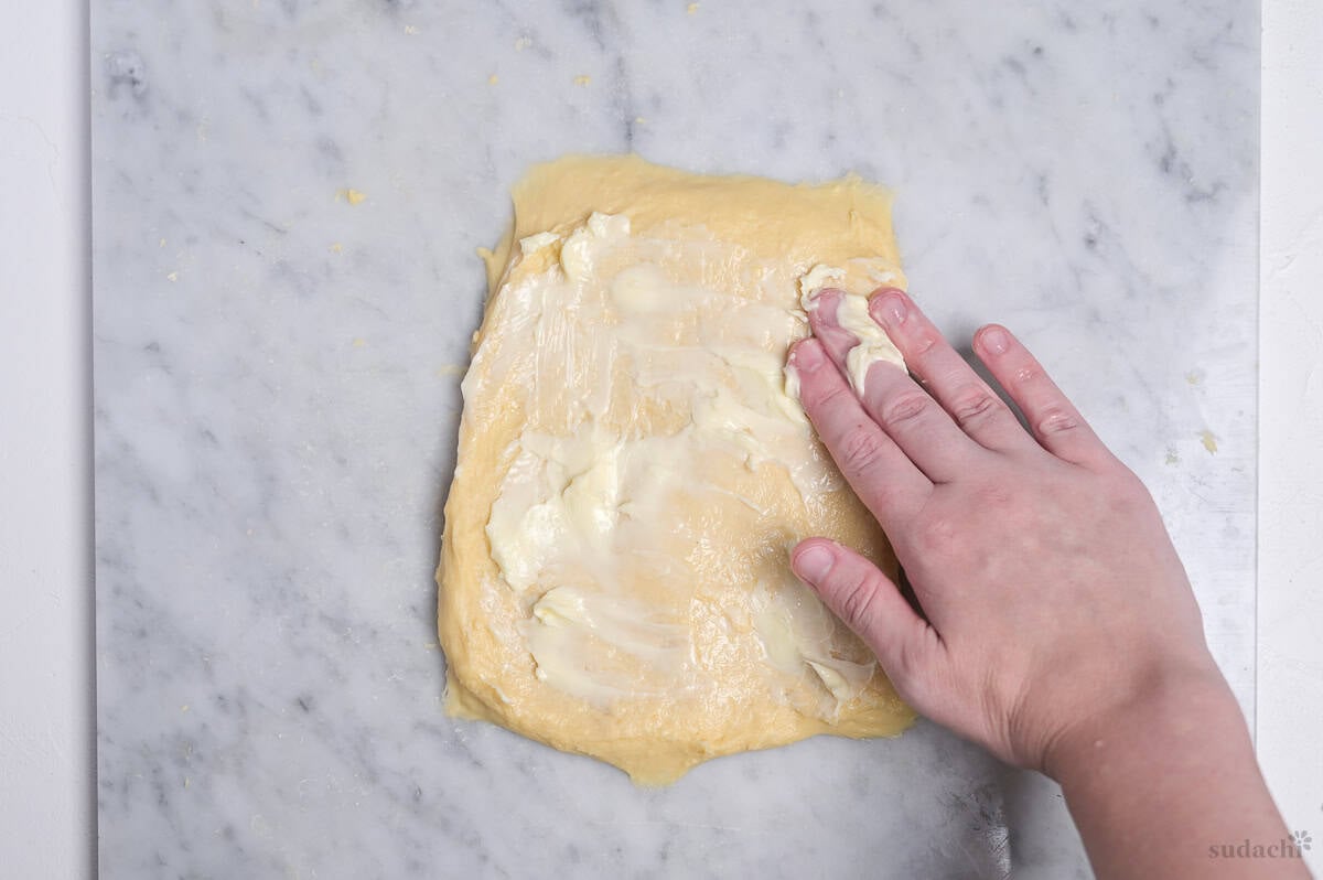 Dough spread out on kneading board with unsalted butter spread over the surface