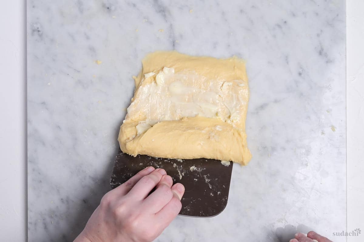 Using bench scraper to roll up the dough and butter