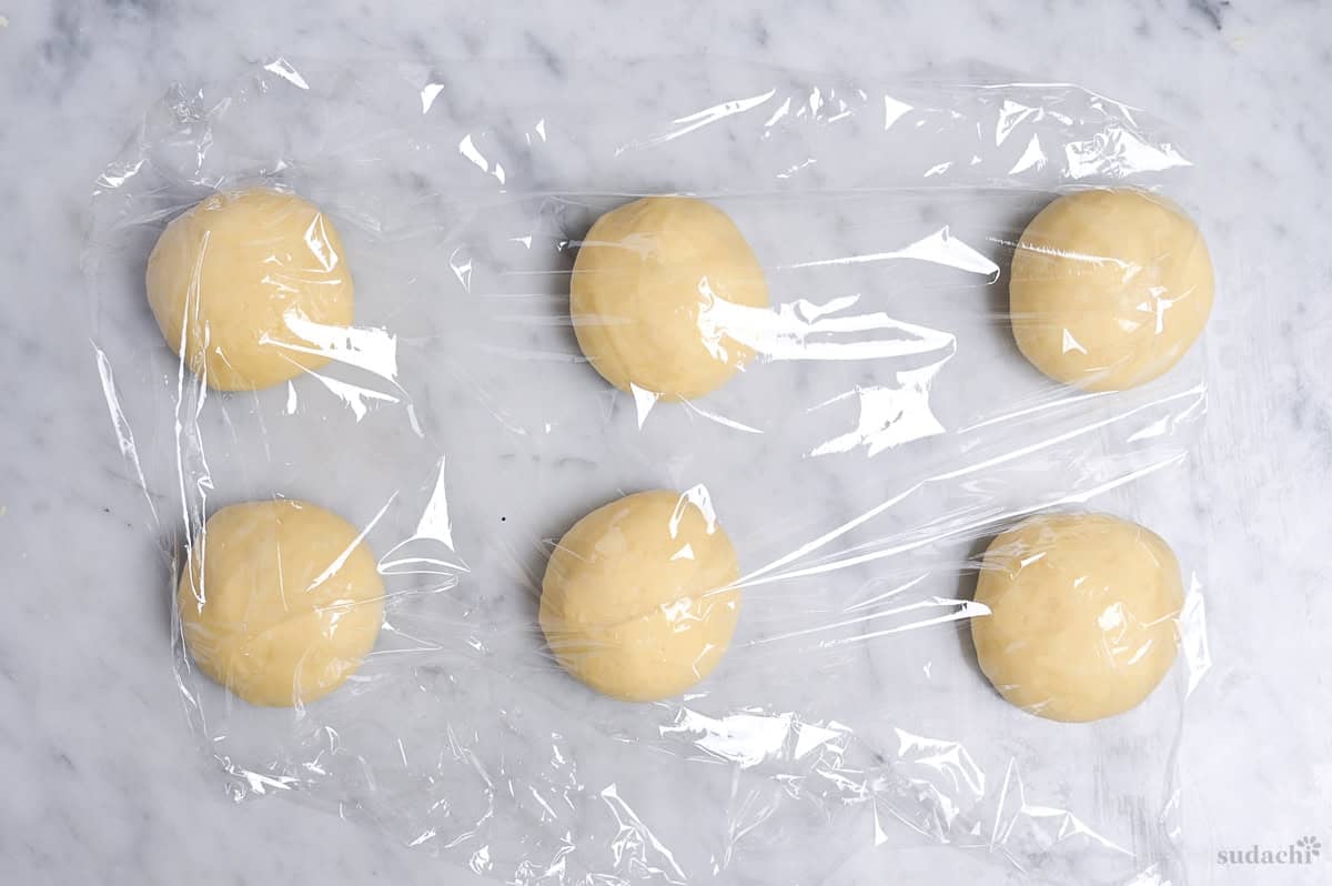6 balls of dough resting under plastic wrap for bench time