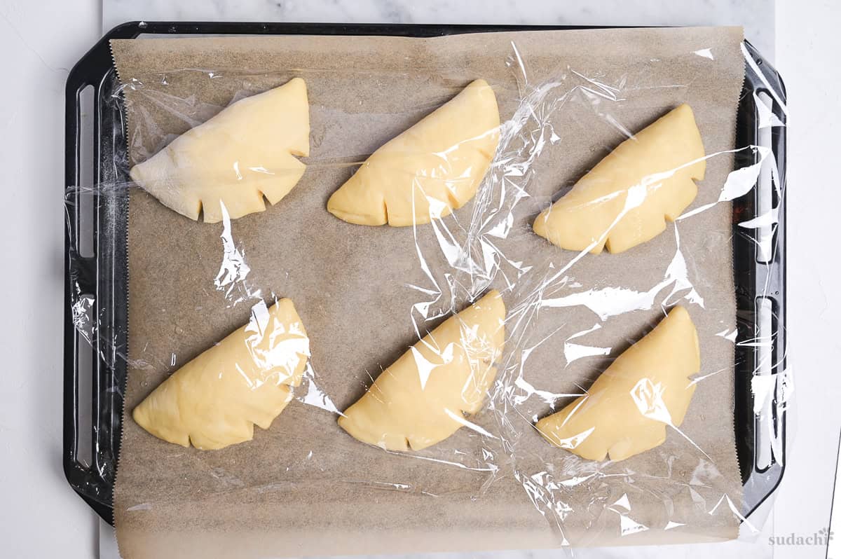 six shaped cream pan on a baking tray lined with parchment paper, topped with plastic wrap. Second rise.