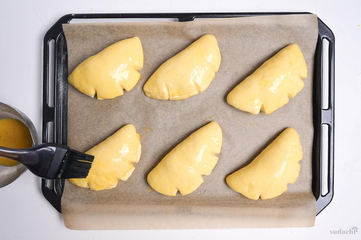 Brushing risen cream pan with egg wash before baking.