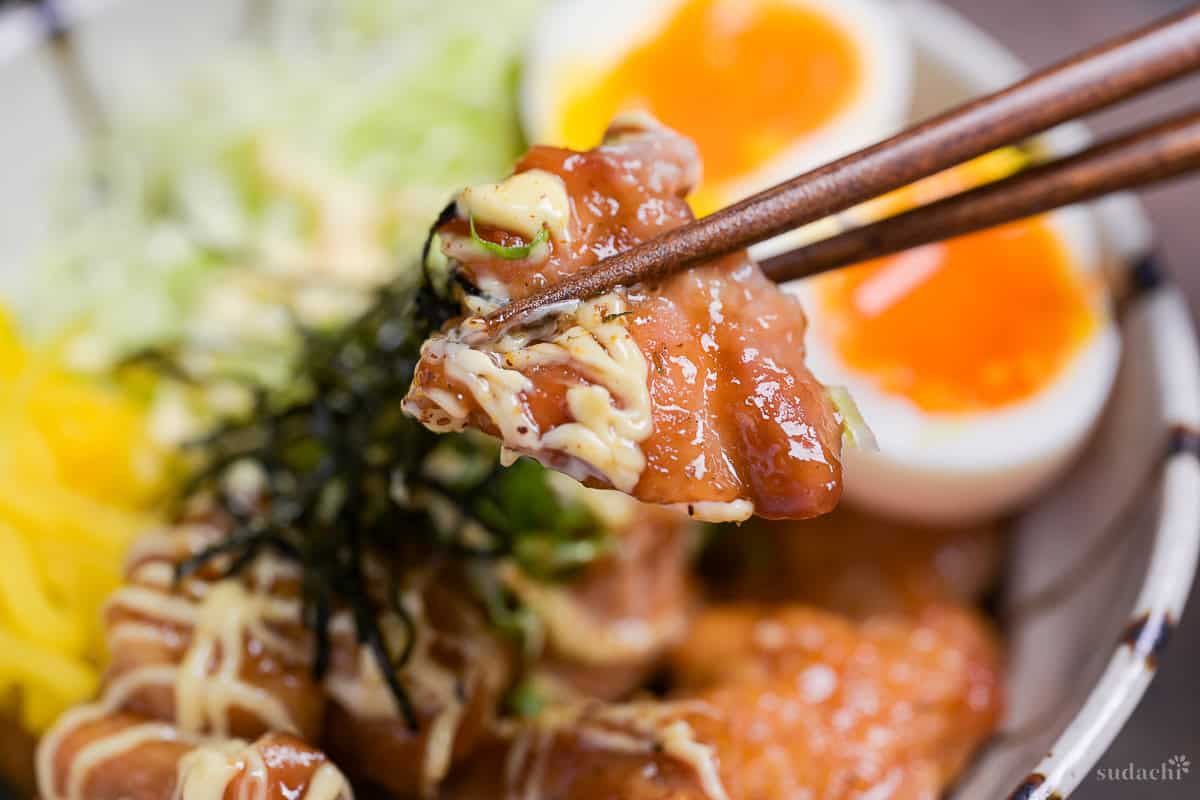 Close up of garlic teriyaki chicken held up with wooden chopsticks