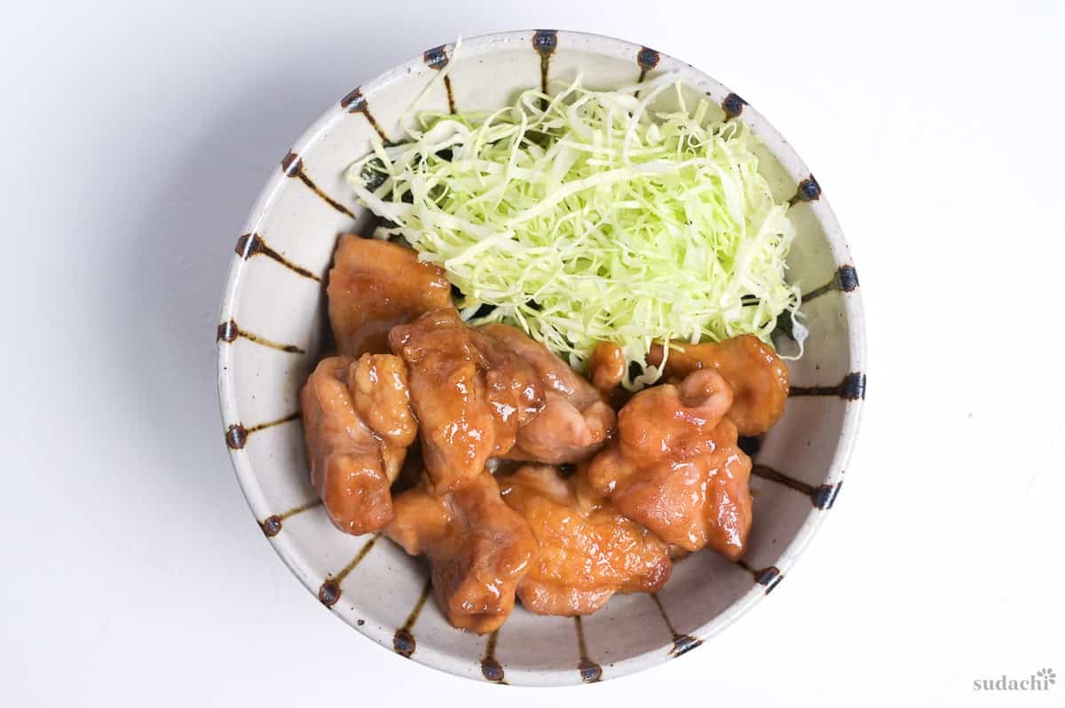 Garlic teriyaki chicken next to shredded green cabbage over rice in a bowl
